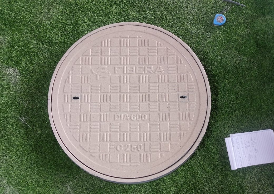 Round, light grey FRP manhole cover installed on a grassy lawn.