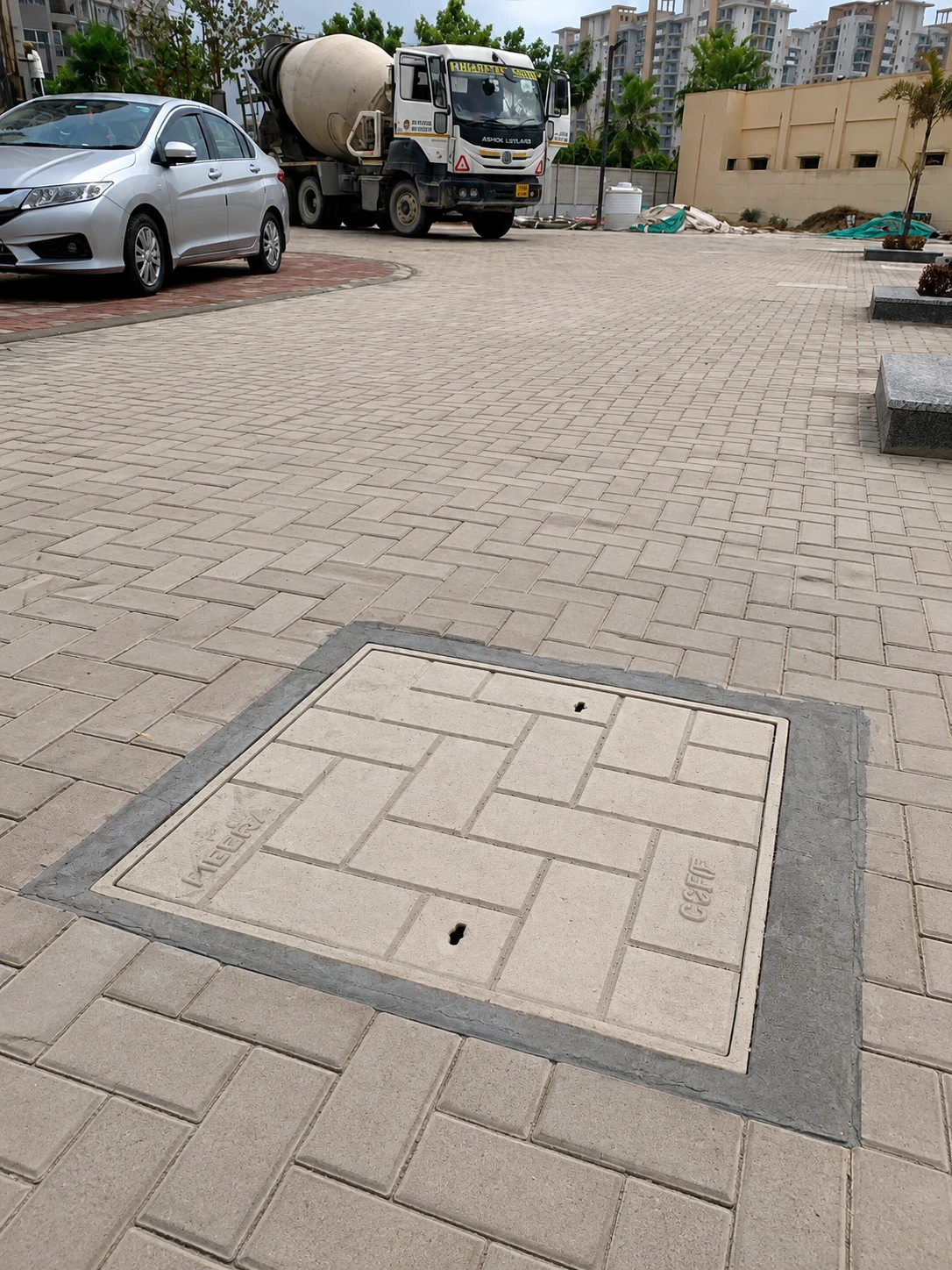 Square grey FRP recessed cover seamlessly blended into patterned stone paving.