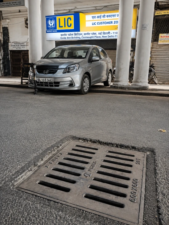 Rectangular FRP drainage cover installed on a street curb near a parked white car.
