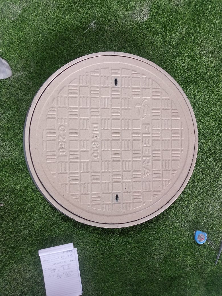 Round, light grey FRP manhole cover installed on a grassy lawn.